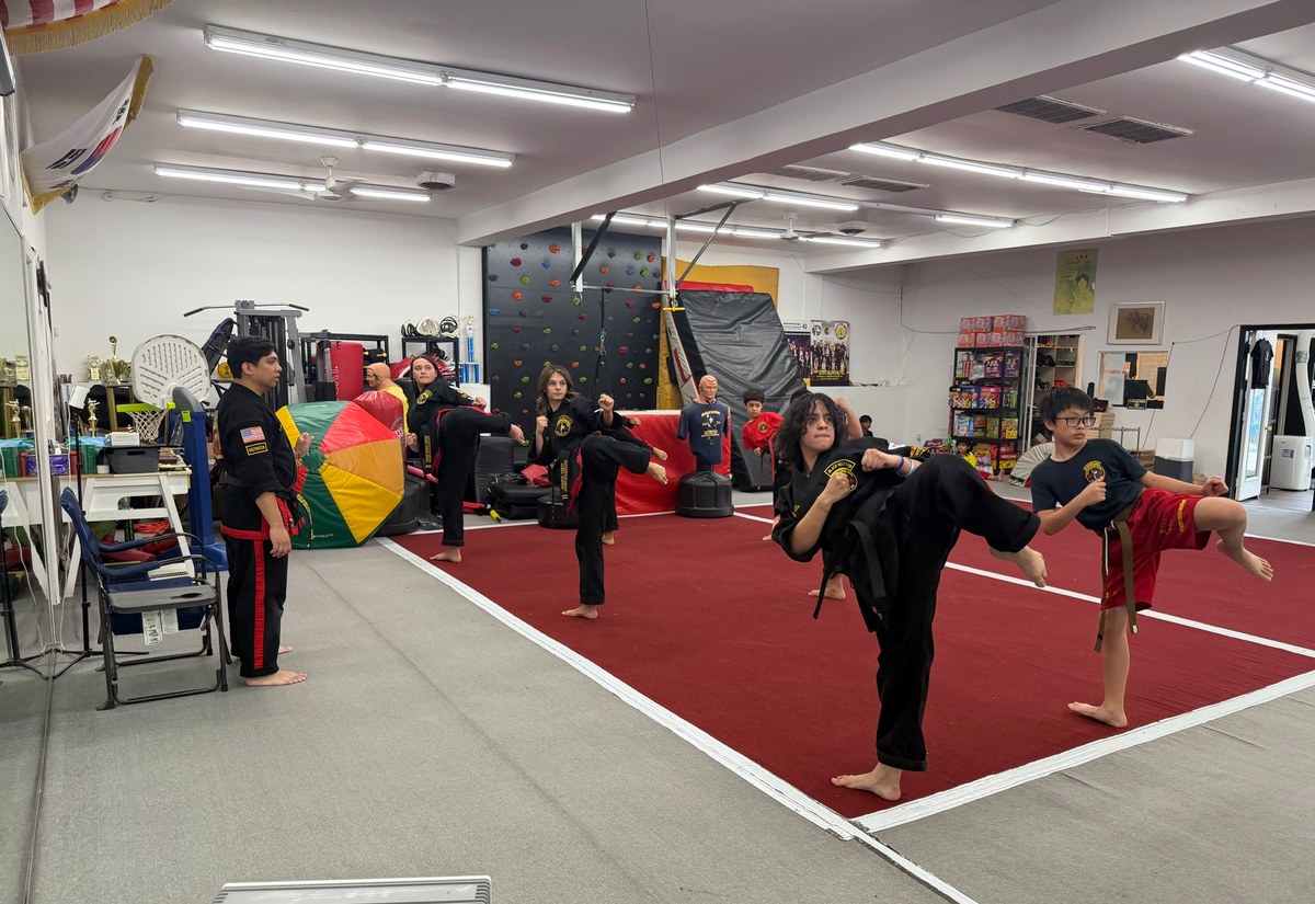 Black-uniform martial artists performing synchronized high kicks.