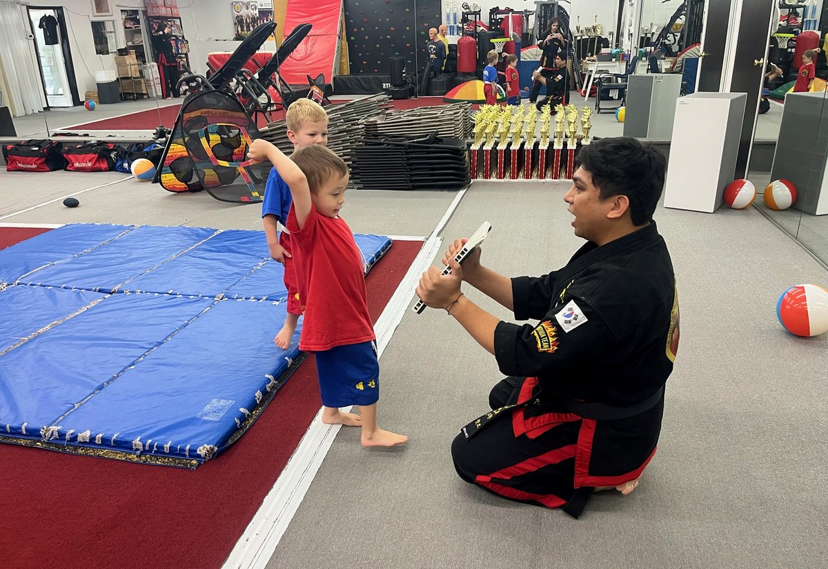 An instructor coaching a student at mat level during a martial arts class.